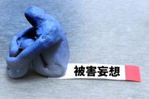 被害妄想という文字と青い落ち込んだ粘土人形
